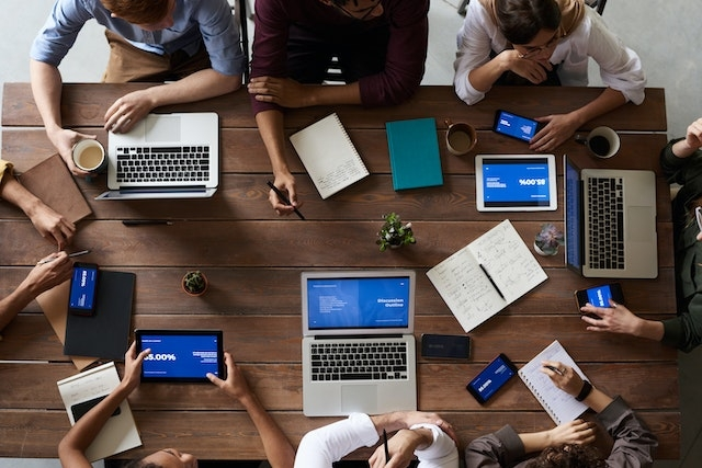 Blick von oben auf einen Besprechungstisch mit Laptops, Kaffeebechern und Notizbüchern, die in geordneter Weise angeordnet sind, während die Teilnehmer an kollaborativen Gesprächen teilnehmen